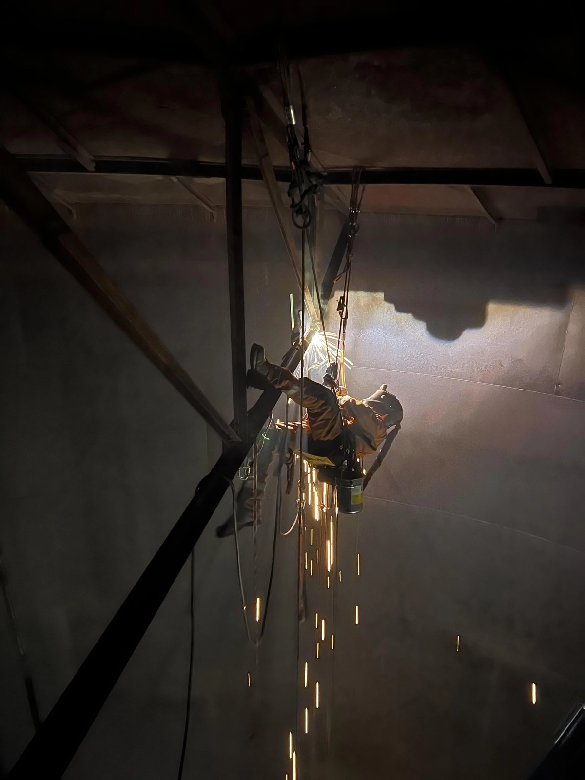 Rope access welder suspended on ropes MMA welding inside a tank, sparks falling below